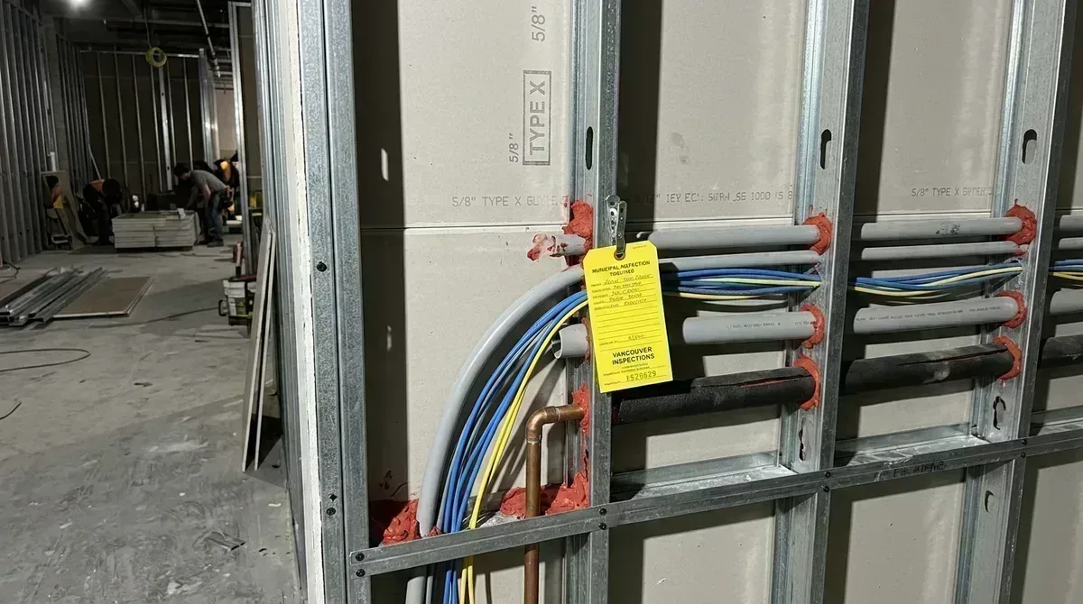 Commercial tenant improvement fire separation demising wall inspection with red firestop collars and municipal inspection tag